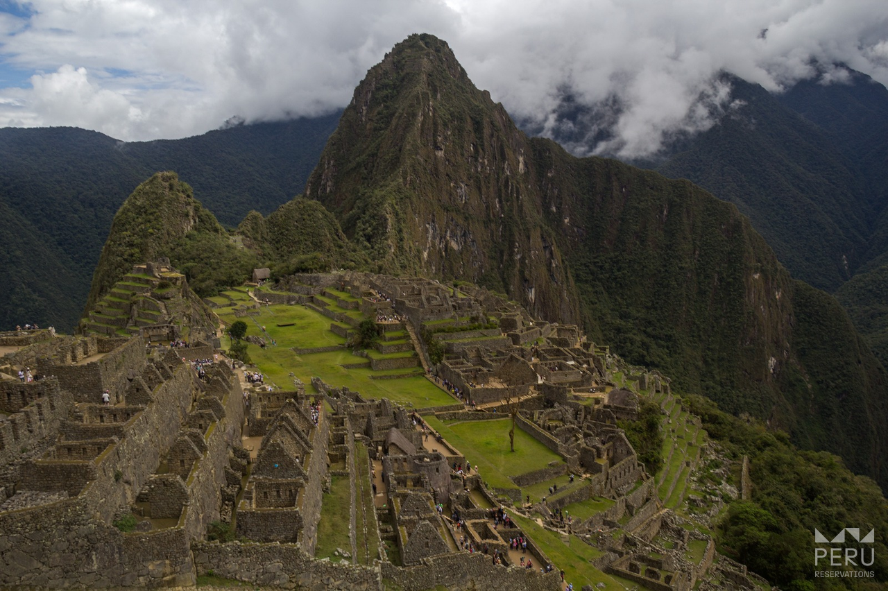 https://www.peru-reservations.com/wp-content/uploads/2025/10/machu_picchu_con_grupo_de_turistas_y_montanas-machu_picchu_with_group_of_tourists_and_mountains.png