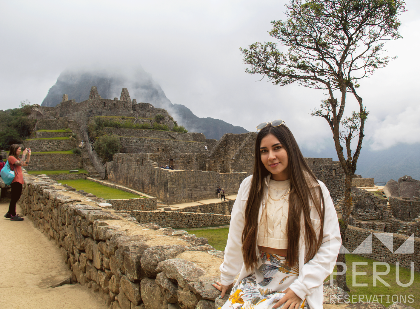 https://www.peru-reservations.com/wp-content/uploads/2025/10/mujer_joven_sentada_en_machu_picchu-young_woman_sitting_at_machu_picchu.png