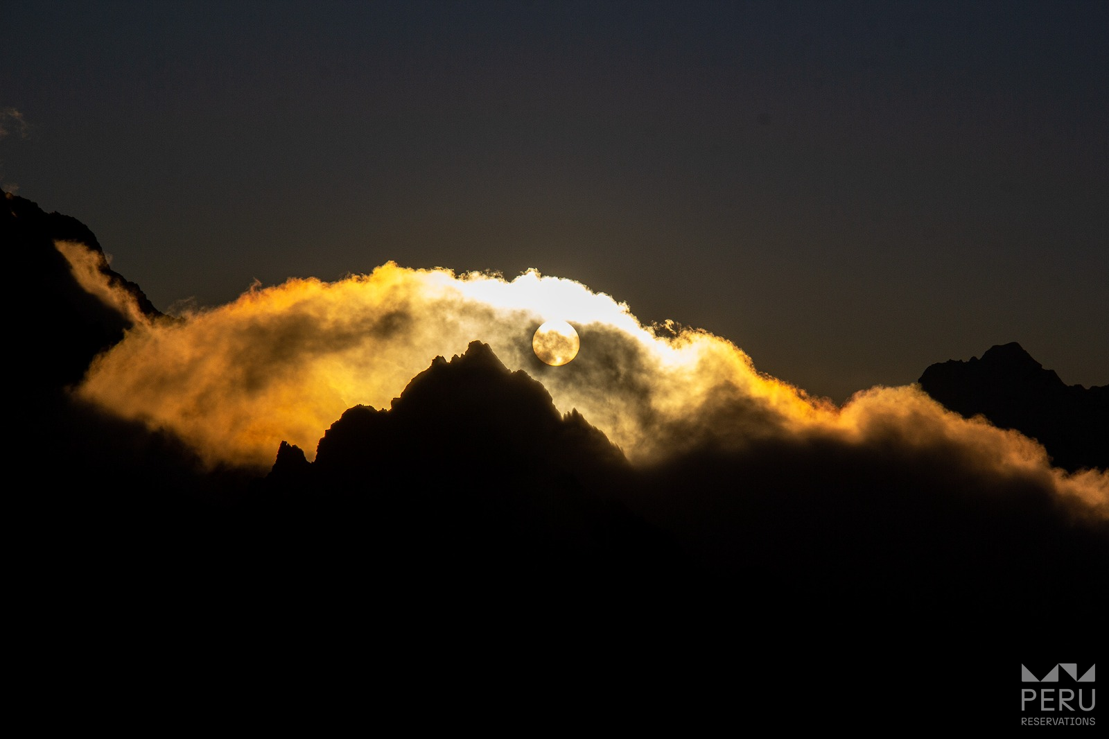 Hidden sun between mountains and clouds at sunset
