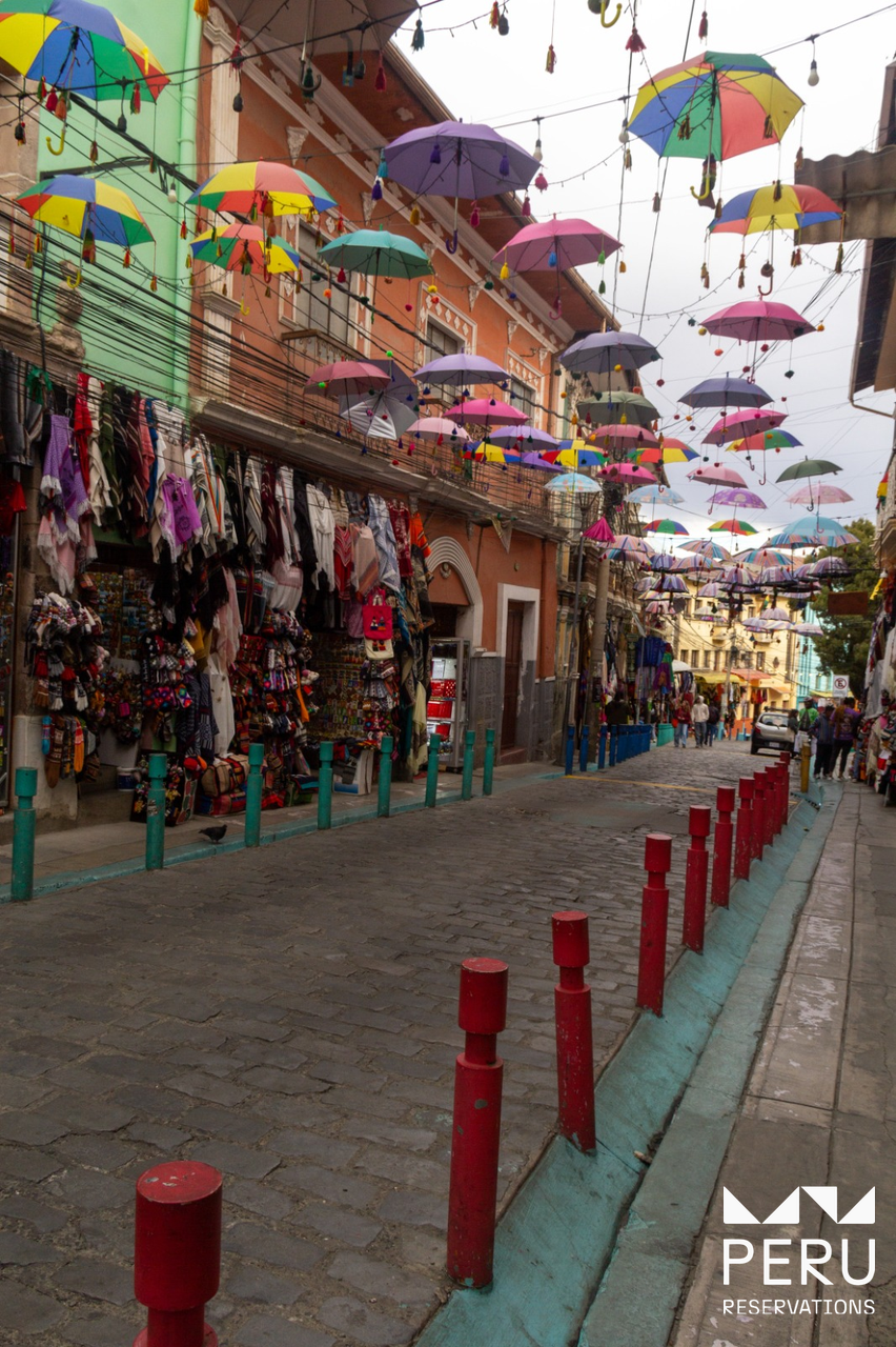Cobblestone street with colorful umbrellas shops and people