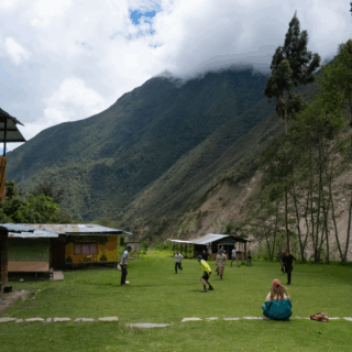 grupo_jugando_fútbol_en_campo_con_cabañas_y_montañas-group_playing_soccer_on_field_with_cabins_and_mountains